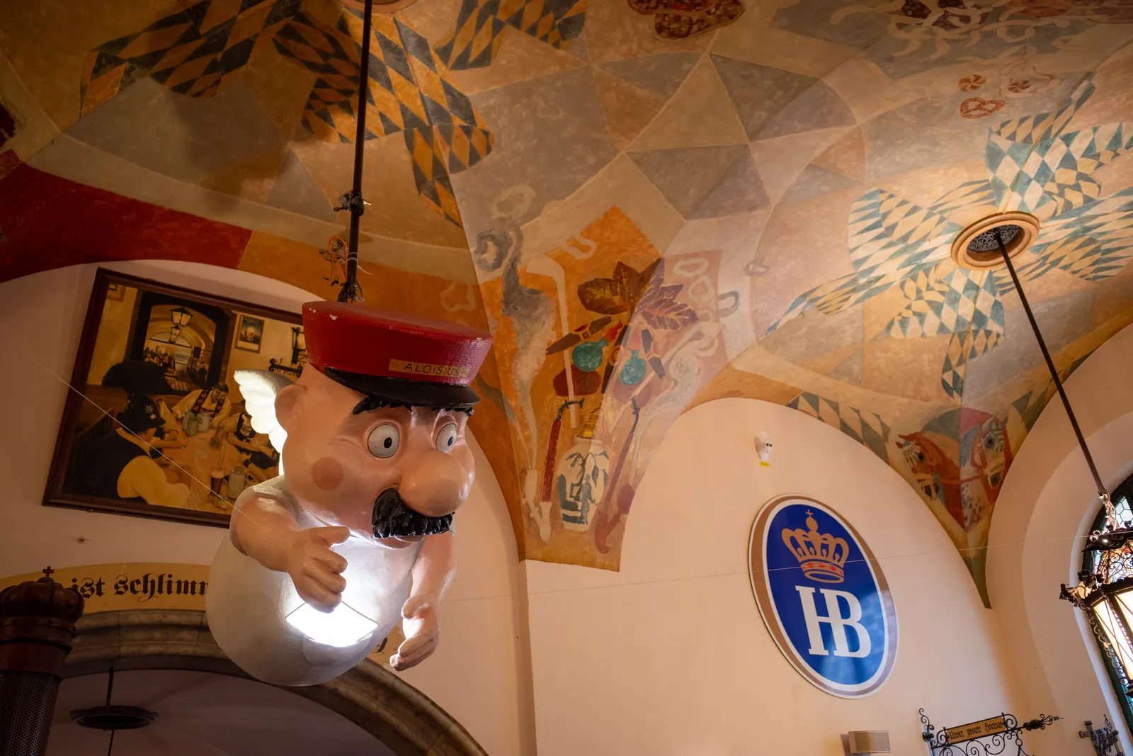 The painted vaulted ceiling and HB roundel of the Hofbräuhaus in Munich, with its mascot figure